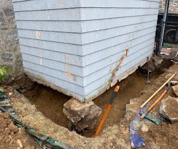 White shed lifted on blocks with exposed ground, orange pipes, and tools at a construction site