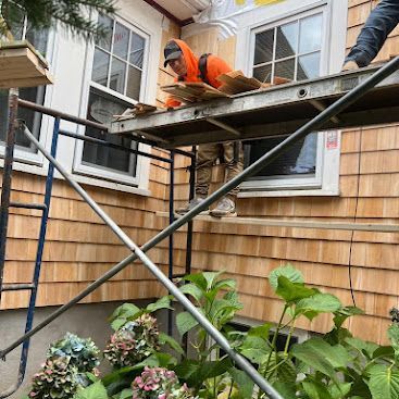 Worker on scaffolding repairing the exterior wall of a house with shingle siding and windows