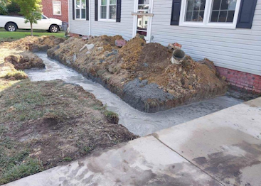 Construction dirt piled along house foundation beside a sidewalk and lawn