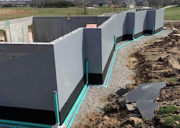 Gray concrete foundation walls under construction with green waterproofing along the base