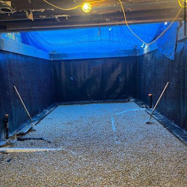 Indoor batting cage with gravel floor, blue netting, and baseball bats leaning on both sides