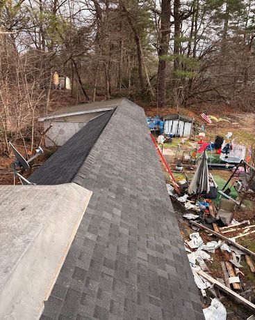 Rooftop under construction beside a wooded yard with scattered tools and debris