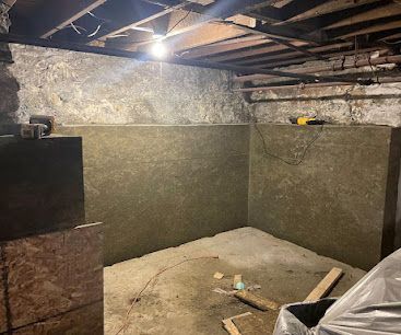 Dim basement with unfinished concrete walls, exposed beams, and a bare dirt floor lit by a single bulb.