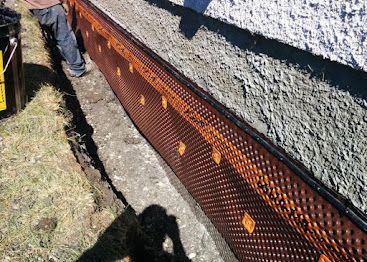Orange mesh gutter guard along a roof edge beside gravel and grass