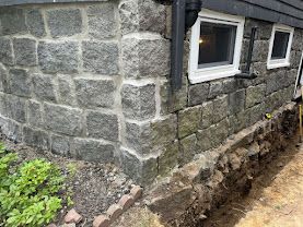 Stone house wall with windows and a dug-up trench along the foundation