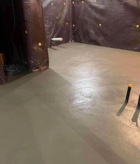 Bare concrete floor in a dark, curtained space with two small protruding pipes near the right edge
