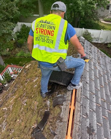 Worker on a roof inspecting storm damage beside a damaged shingle seam and ladder.