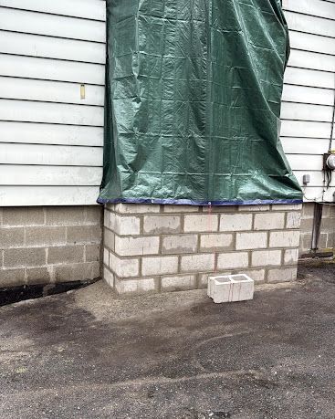 Covered doorway on a white house with cinderblock base; a small stack of blocks sits on the driveway.