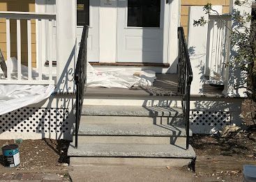 Front porch steps with black metal railings leading to a white front door.