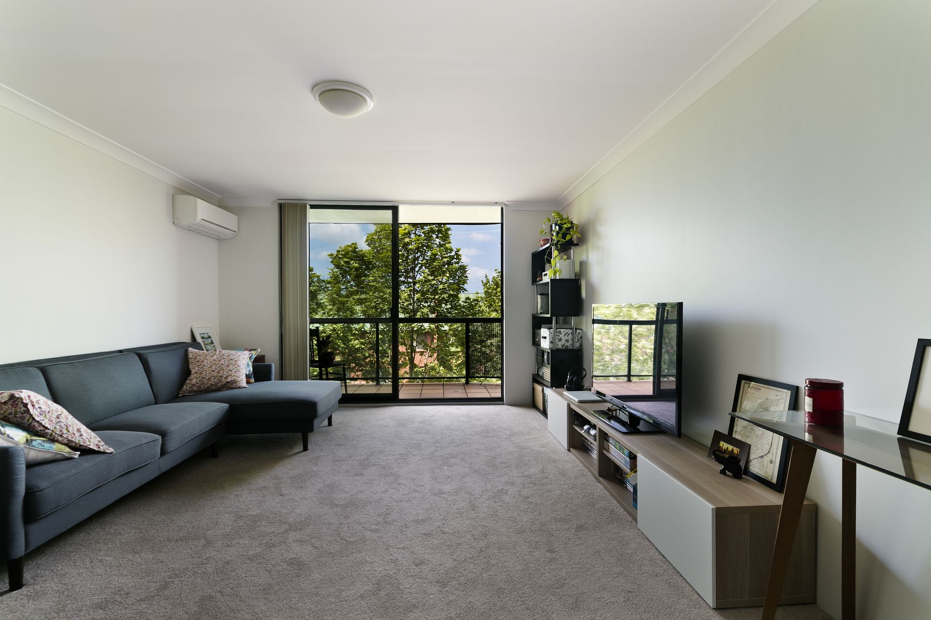 Living room with gray sofa, sliding glass doors to a balcony, and a TV on a modern cabinet.