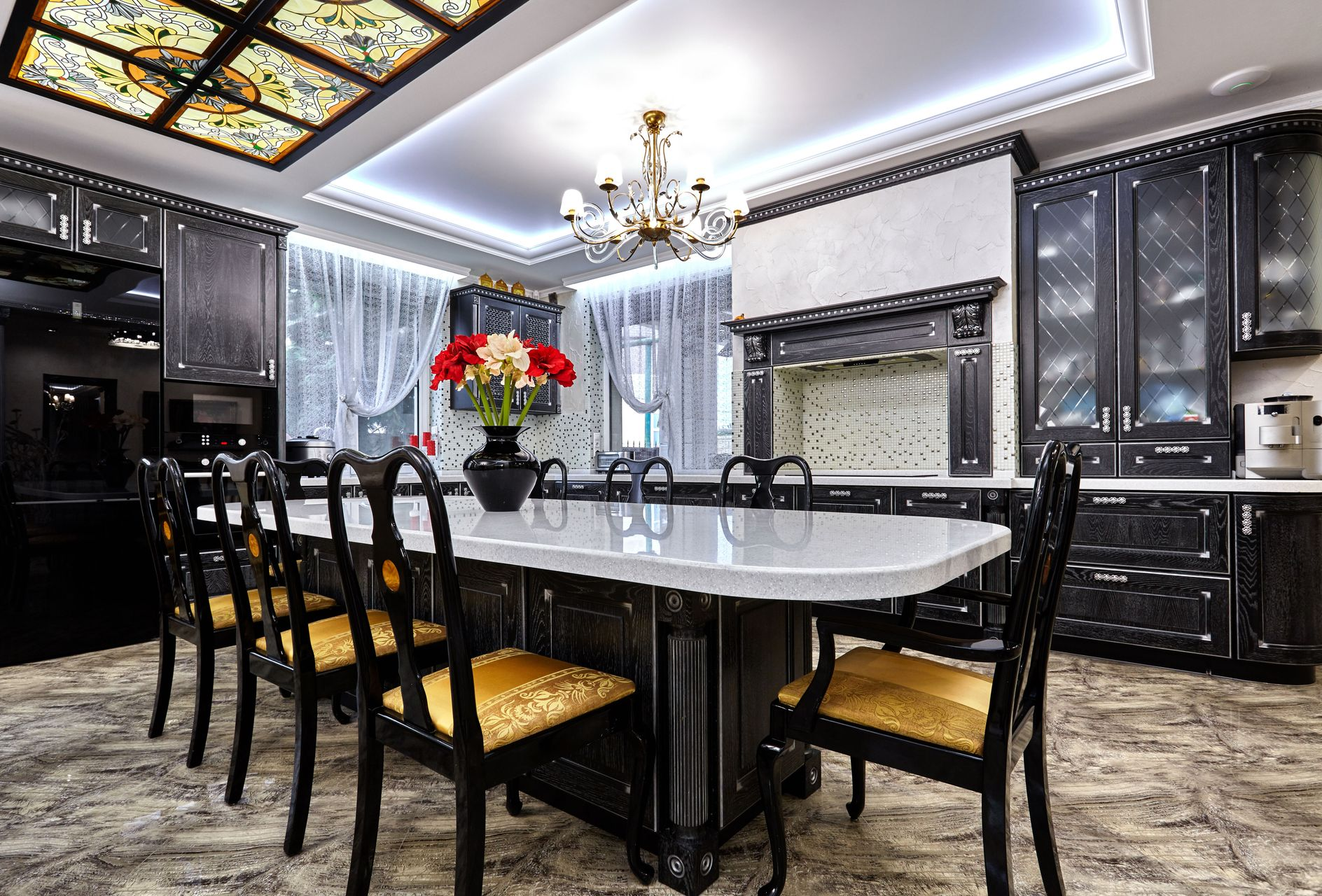 Elegant black kitchen with dining table and chairs, chandelier, and a colorful floral arrangement.