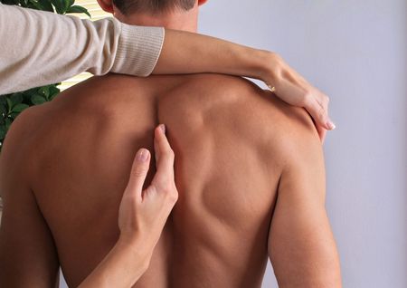 Person's bare back being examined by two hands, possibly for a medical checkup, indoors.