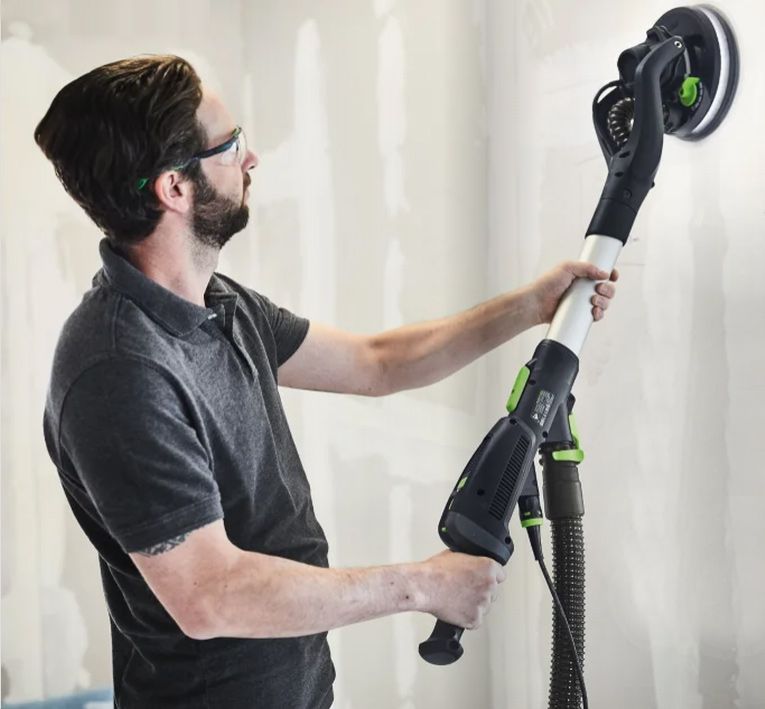 A man wearing glasses is using a sander on a wall