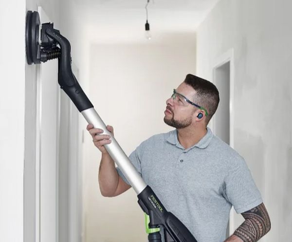 A man wearing glasses is using a sander on a wall