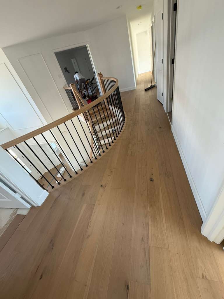 Interior hallway with a curved stair railing and beige carpet leading to open doorways - After