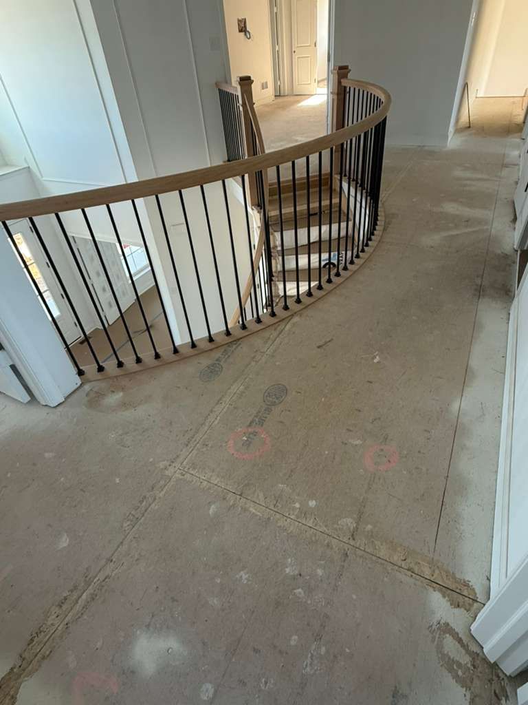 Interior hallway with a curved stair railing and beige carpet leading to open doorways - Before
