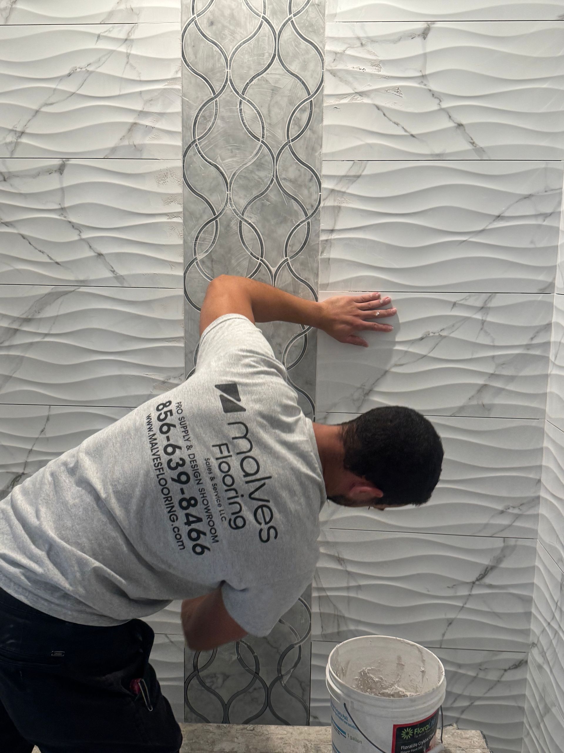 Worker smoothing plaster on a textured wall with a metal trowel next to a bucket of material