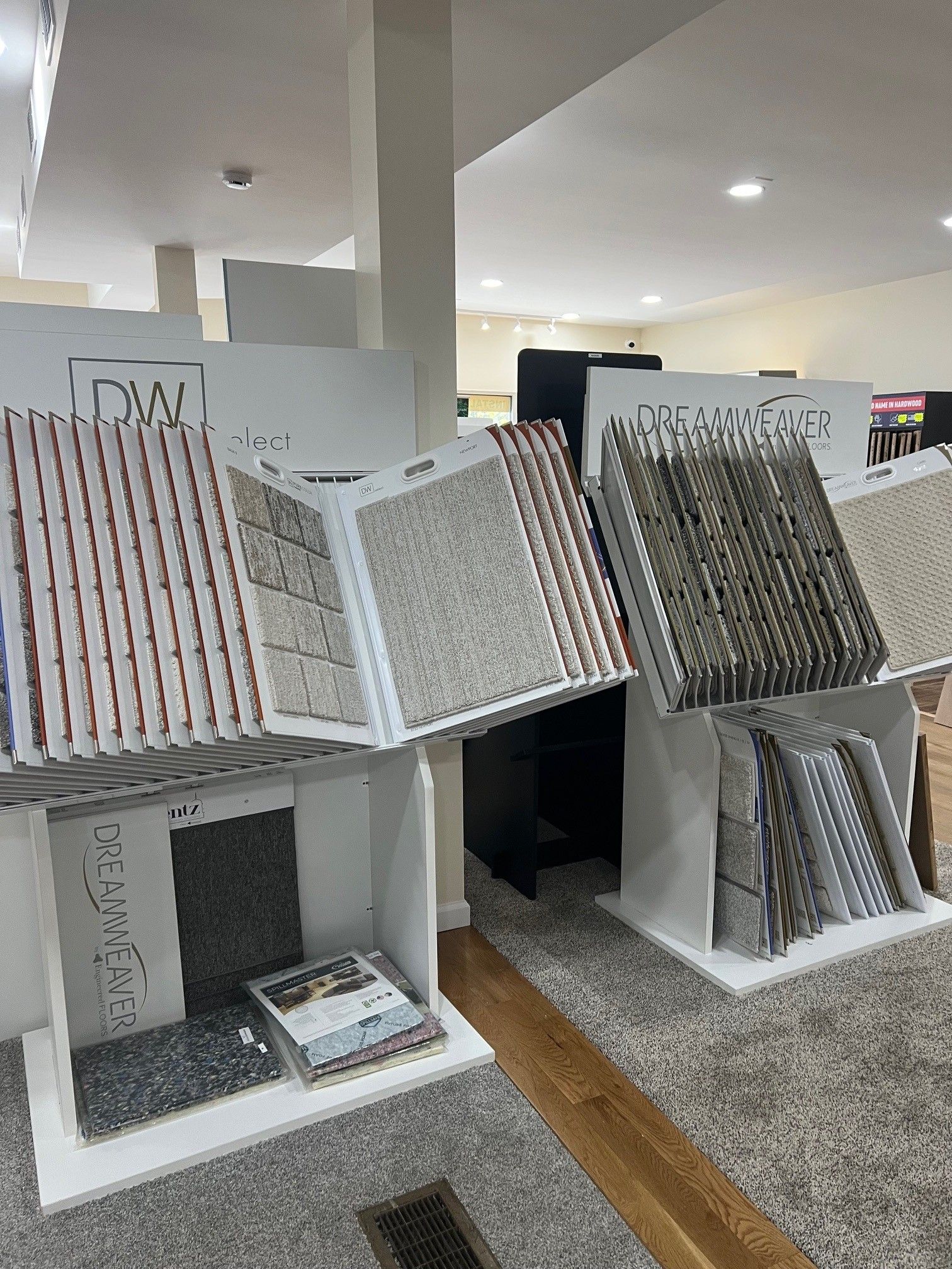 Display of patterned wallpaper samples on white shelves in a showroom, with assorted rolls and swatches.