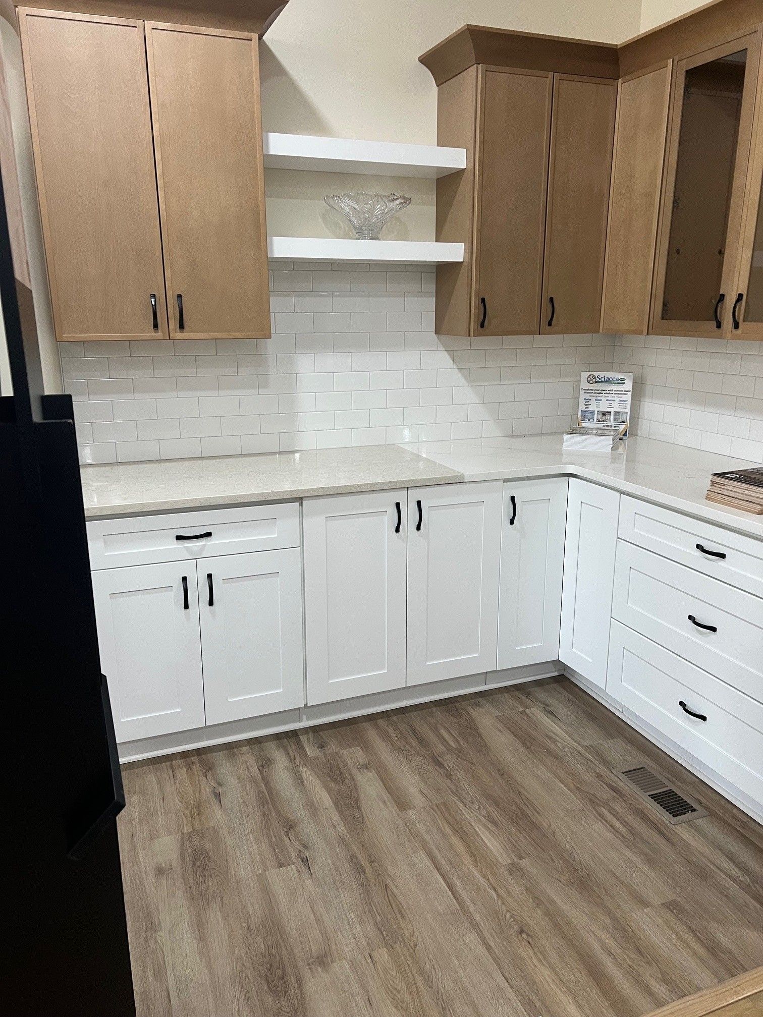 Bright kitchen with white cabinets, wood upper cabinets, white tile backsplash, and wood-look flooring