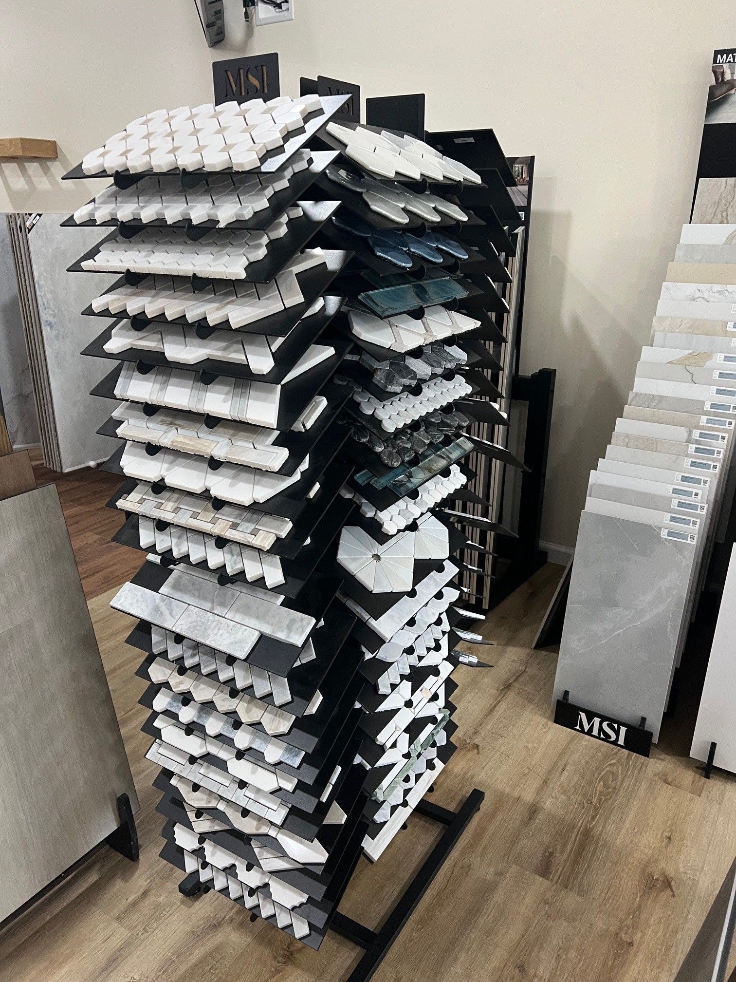 Tall rotating display rack with rows of white trays in a room with wooden floors.