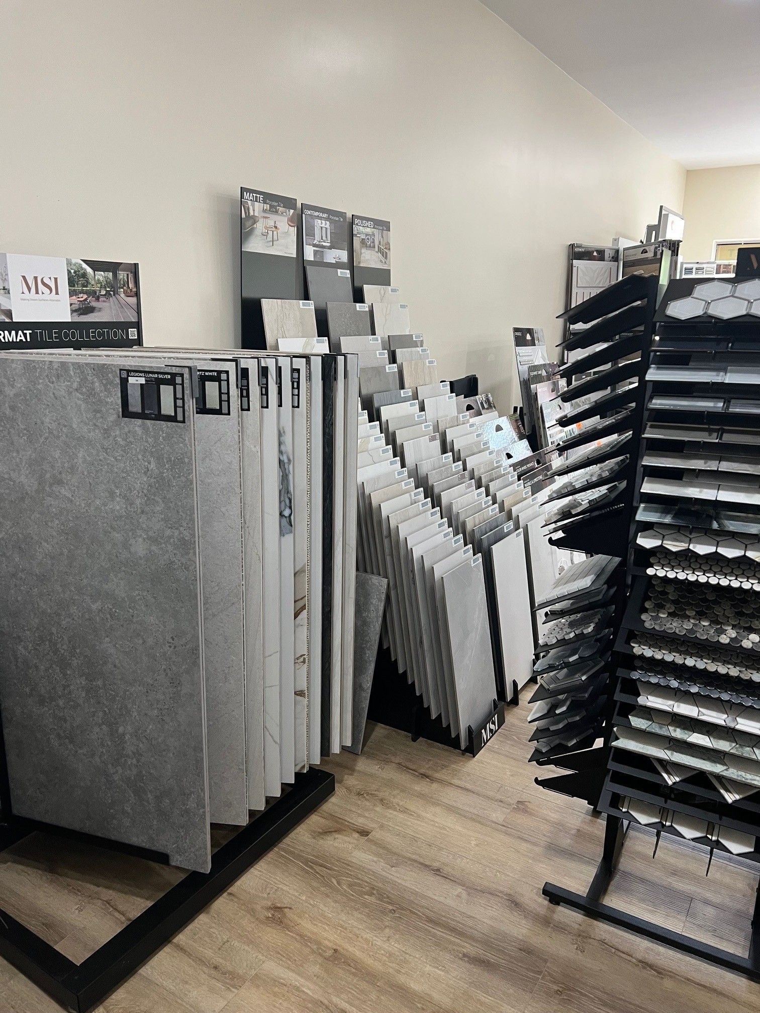 Showroom with stacked tile and flooring samples displayed on racks along a beige wall.