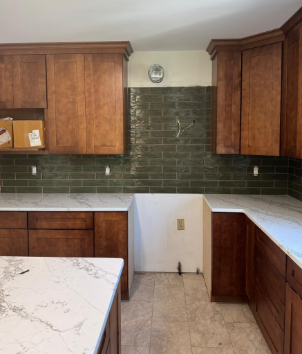 Empty kitchen with wood cabinets, dark green backsplash, and white countertops.