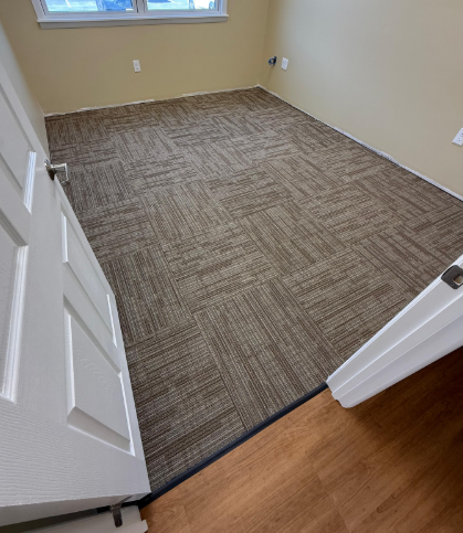 Empty beige room with brown carpet and an open door leading to hardwood floor.