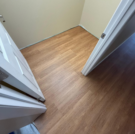 Empty hallway corner with light wood flooring and beige walls, viewed from an open doorway