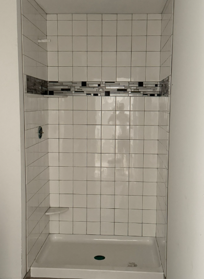 White tiled shower stall with a built-in shelf and shower pan drain
