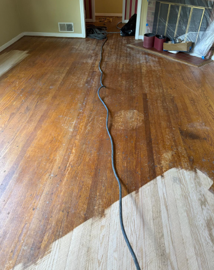 Damaged hardwood floor with a long black cord running through the room and a large peeled, unfinished patch