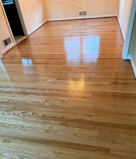 Empty hardwood-floored room with beige walls and bright window reflections