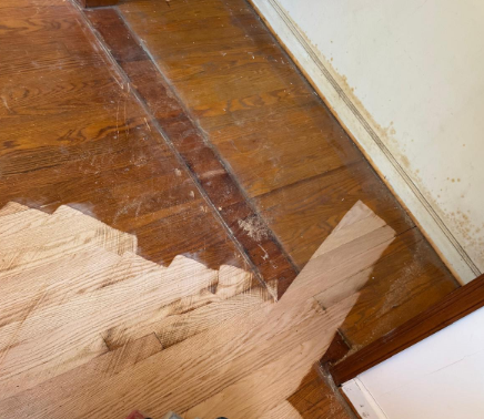 Damaged wooden floorboards with peeling finish beside a white wall and baseboard