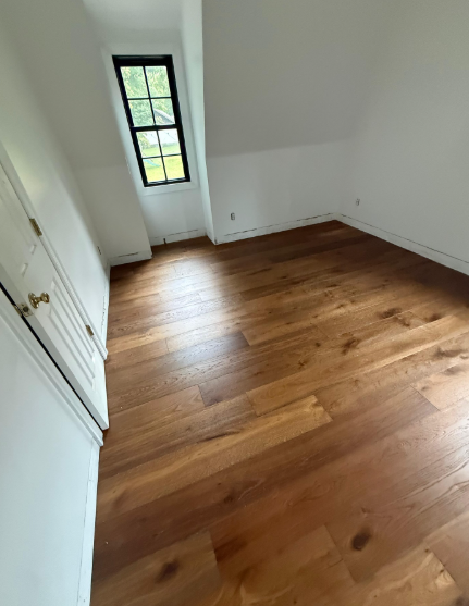 Empty white room with wood floors and a tall narrow window at the far wall