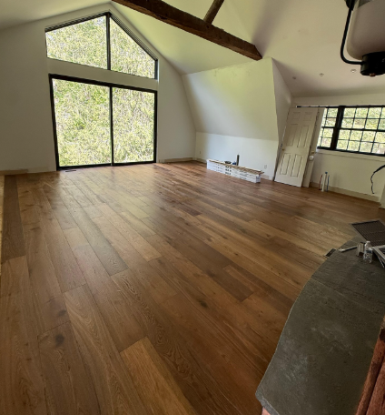 Empty attic room with hardwood floors, slanted ceiling, large triangular window, and exposed beams