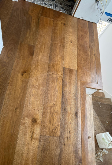 Wooden tabletop or floorboards with a warm brown finish next to a white wall and small white object