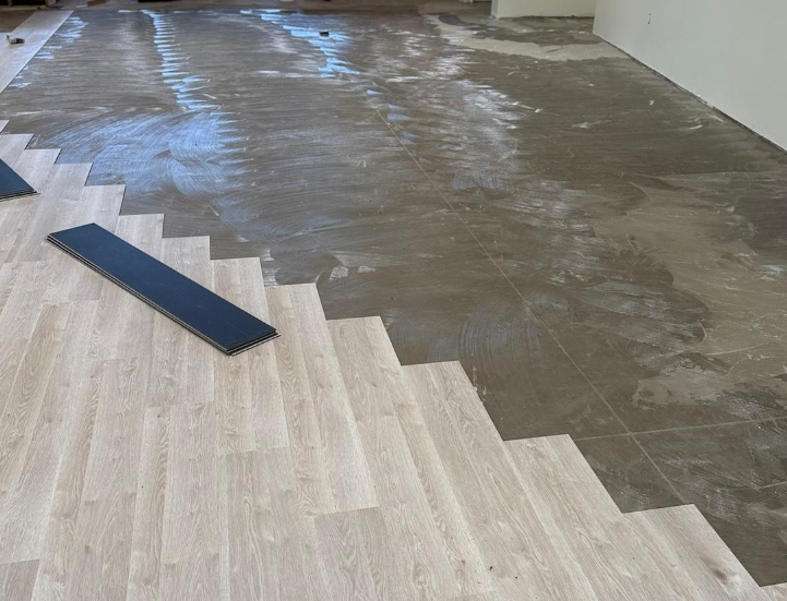 Partially installed wood-look floor beside a wet concrete subfloor, with a dark strip on the floor