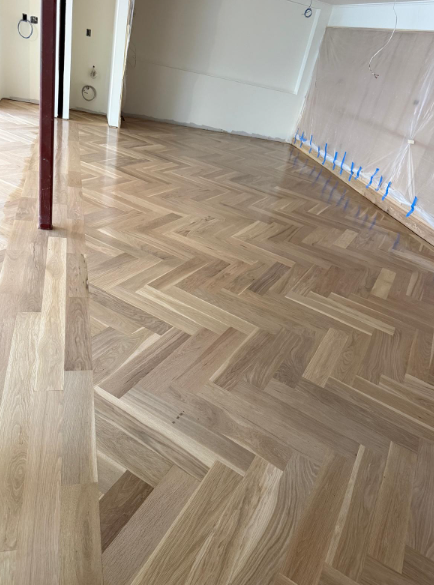 Empty room with herringbone wood floor and a wall lined with blue protective tape