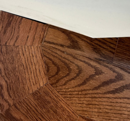 Close-up of a hardwood floor corner with a white wall trim above it