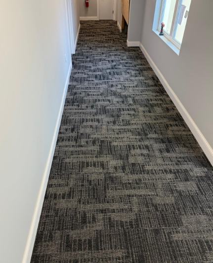 Narrow hallway with gray patterned carpet, white walls, and a window on the right.