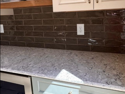 Kitchen countertop with speckled granite, dark tile backsplash, and white cabinet above.