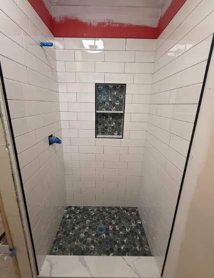 Small tiled shower stall with blue fixtures, dark mosaic floor, and a small window.