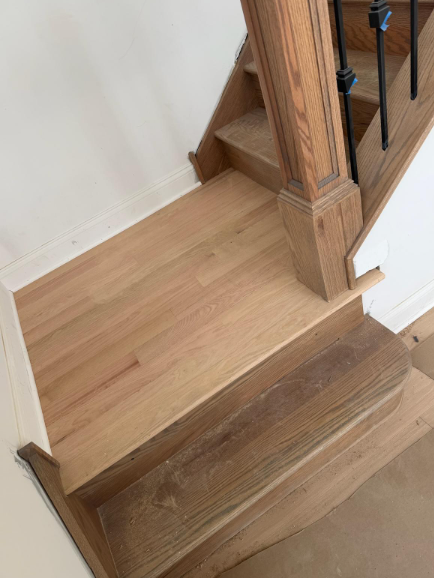 Wooden staircase landing with light wood flooring and a railing beside a white wall