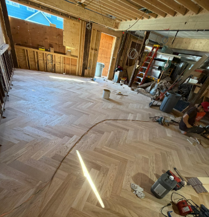 Unfinished room with light wood herringbone floor, exposed walls, and construction tools during renovation