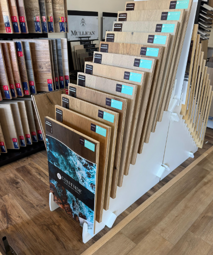 White display rack holding multiple brown carpet samples with turquoise labels in a store.