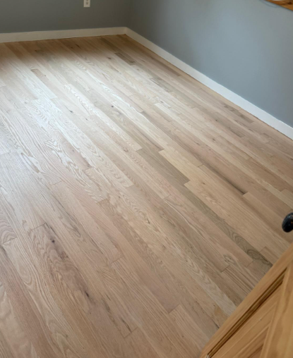 Empty room with light wood flooring, gray walls, and white baseboards