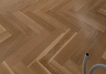 Herringbone wood floor with part of a gray vacuum hose in the lower right corner