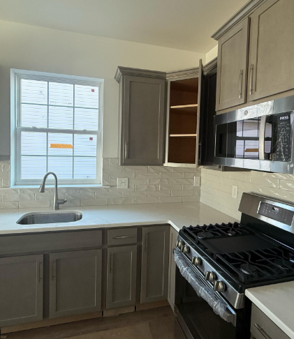 Modern kitchen with gray cabinets, white countertops, window over sink, and stainless steel stove and microwave.