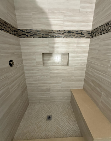 Empty tiled shower with bench, drain, and small recessed shelf.