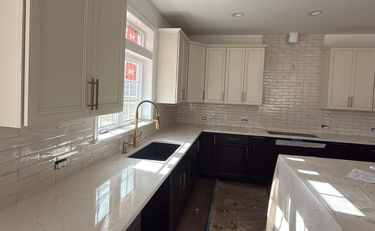 Bright kitchen with white cabinets, dark lower cabinets, marble counters, and a subway-tile backsplash