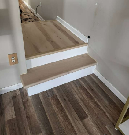 Carpeted step up to a light wood landing in a hallway with white walls and dark wood flooring